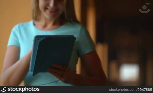 Tilt shot of a woman using a touchpad standing by the window in the hall