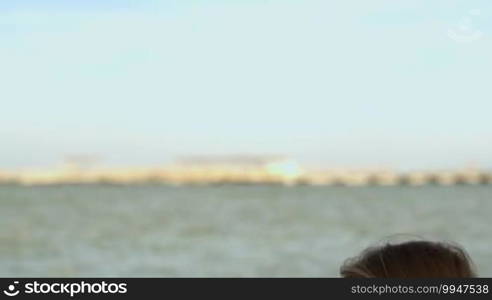 Tilt shot of a young woman in sunglasses typing on a tablet computer sitting by the sea