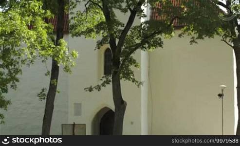 Tilt shot of old Catholic church with high cone roof and green trees