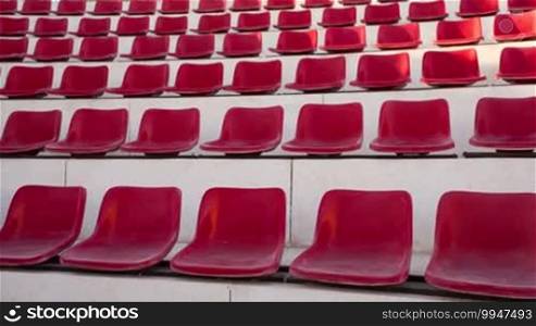 Tilt shot of rows of vacant red seats at the sports stadium