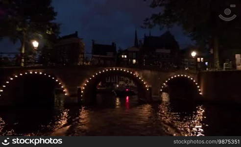 Time lapse view of night cityscape during river cruise on moving boat, buildings with lights, cars on the waterfront, Amsterdam, Netherlands