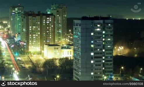Timelapse and high angle shot of illuminated big city at night. Multistorey houses with window lights on and off and intense traffic