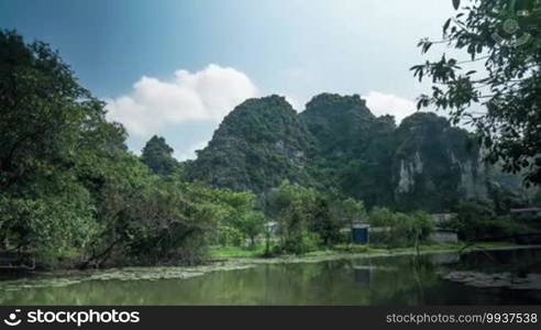 Timelapse in Vietnam. Seen a scenic view of river, trees and mountains, and in the blue sky floating clouds.