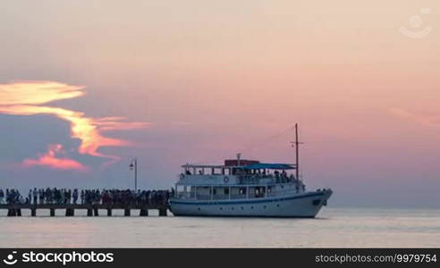 Timelapse of touristic ship sailing to pier, unboarding and boarding passengers and pushing off. Sea travel at sunset