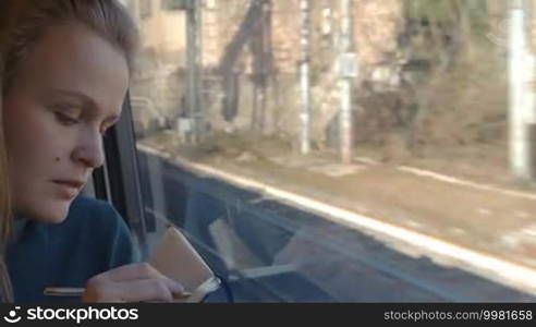 Timelapse of young woman traveler writing or drawing in sketchbook while she is traveling by train and looking out the window