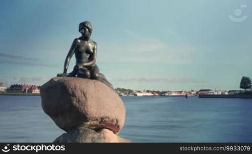 Timelapse shot of boats and ships sailing on the water behind the Little Mermaid statue, some tourists taking picture with it