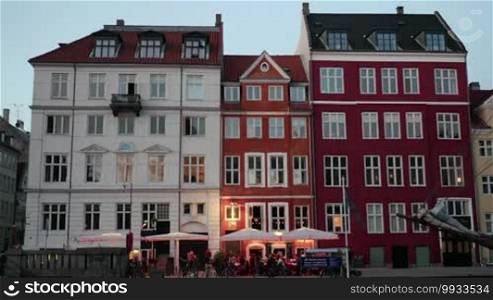 Timelapse shot of evening coming to the city. View of the classic style building facades in white and red colors with an outdoor cafe and parked bikes nearby, people passing by