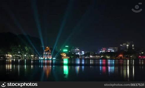 Timelapse shot of Hanoi at night. Illuminated Turtle Tower and Hoan Kiem Lake in city center. Colorful lights reflecting in dark water, Vietnam