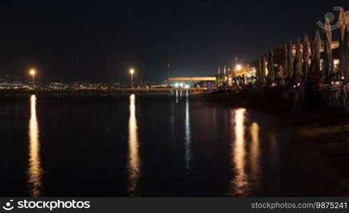 Timelapse shot of nightlife in resort town. People walking on the pier and spending time in beach cafes. Thessaloniki, Greece