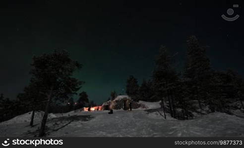 Timelapse shot of people gathering outside by the fire to look at beautiful natural phenomenon - polar lights. Rovaniemi, Finland