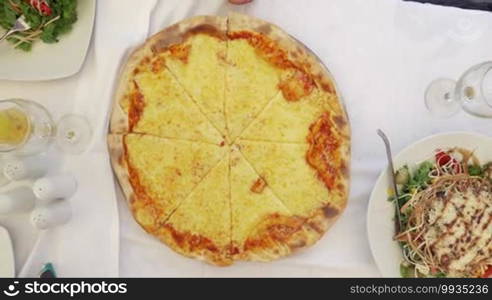 Top view of family taking slices of appetizing cheese pizza served in outdoor cafe