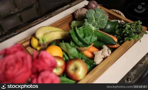 Top view of fresh fruits and vegetables in a wooden tray on a kitchen table close-up. Selective focus on a bouquet of red roses. Top view close-up. Organic food for a healthy lifestyle.