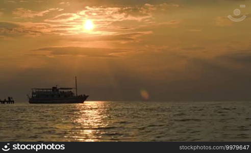 Tourist ship sailing from pier at sunset, some people leaving there