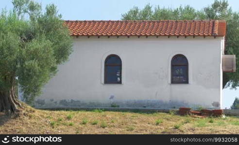 Traditional small house between green trees on a sunny day in Greece