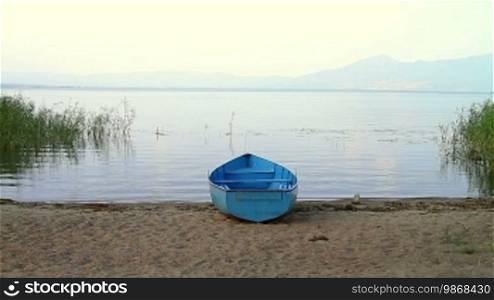 Tranquil landscape with small blue wooden fishing boat parked on lake beach