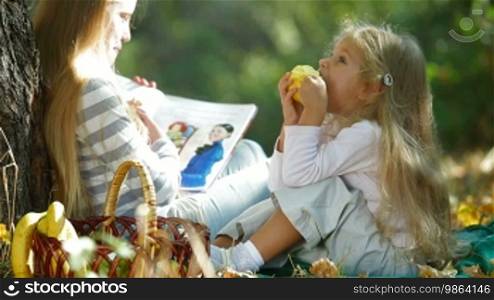 Two blonde little girls reading a book in autumn park