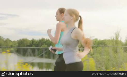 Two girls with a phone in their hands run along the walkway in the park next to the beautiful lake, stop and looking at the mobile phone