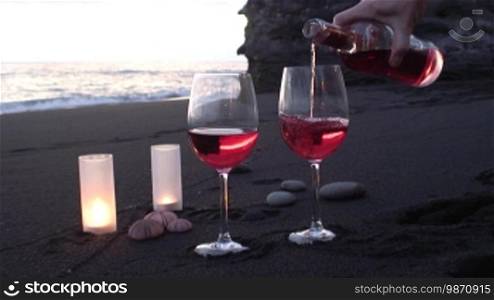 Two glasses of wine being poured on a beach