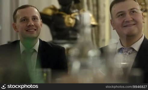 Two men sitting at the table during celebration. They applauding and smiling.