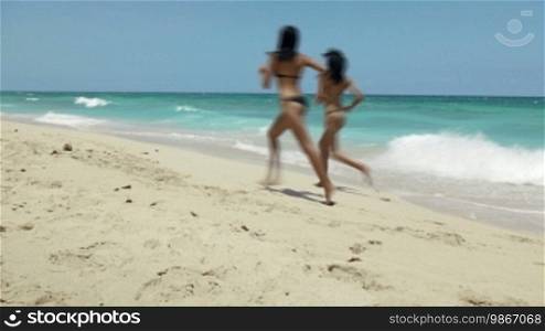 Two pretty Latina sisters in bikinis having fun on the beach near the Caribbean Sea