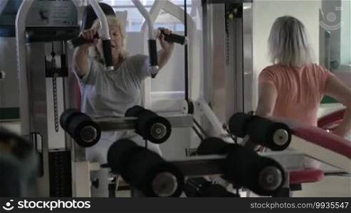 Two senior women working out on exercisers in fitness center. One person using chest press machine and the other pull back machine