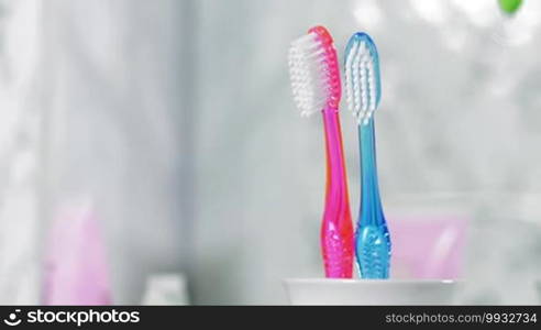 Two toothbrushes are standing in the holder, unseen person is adding a child toothbrush into it. Child birth concept.