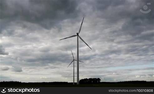 Two wind turbines are in motion against an impressive sky