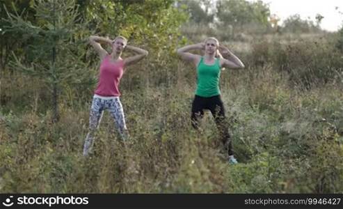 Two young girls training together outdoors: body bent exercises.