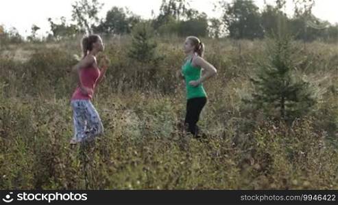 Two young girls training together outdoors: running and jumping exercises.