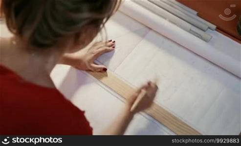 University student of Interior Design doing homework, completing housing project for final exam. The girl draws lines on a blueprint with a ruler in her studio. Close-up, dolly shot