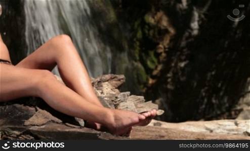 Unrecognizable woman in bikini sunbathing near a waterfall
