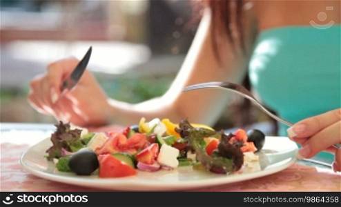 Unrecognizable young woman has dinner in restaurant, Greek salad