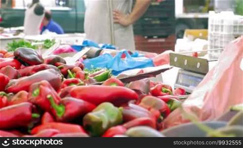 Vendors selling red sweet pepper on street market. Woman paying for vegetables, getting change and taking the packet. Seller adding peppers on the stall