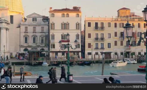 Venetian Grand Canal with water transport, old buildings and people walking along it