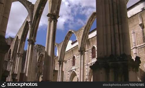 Verzierte Rundbogen Tore aus Stein einer alten Kathedrale im Hintergrund das Gebaude der Kathedrale weiße Wolken ziehen am blauen Himmel.