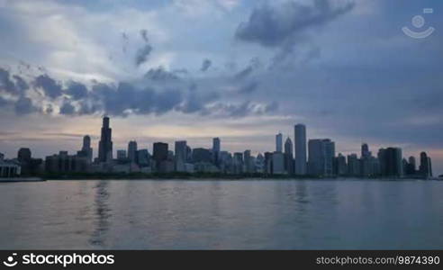 Video time lapse of Chicago downtown skyscrapers reflected on the Michigan lake from sunset clouds motion to night. Awesome Chicago city center skyline at night in the United States of America. Illuminated skyscrapers of Chicago in Spring twilight. Chicago sky in the evening with the sun on the city sky.