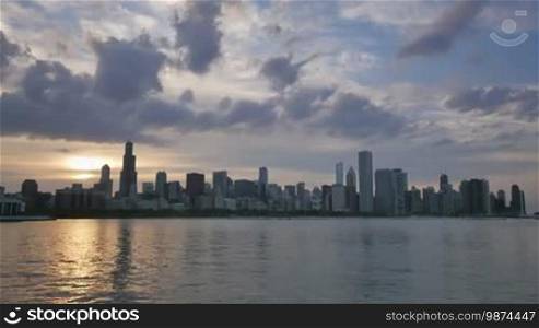 Video time lapse of Chicago downtown skyscrapers reflected on the Michigan lake from sunset clouds motion to night. Awesome Chicago city center skyline at night in the United States of America. Illuminated skyscrapers of Chicago in Spring twilight. Chicago sky in the evening with the sun on the city sky.