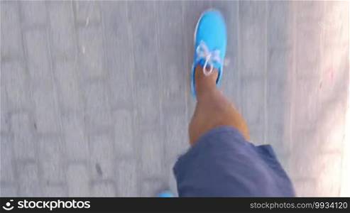 View from above on man's legs in shorts and blue moccasins walking the street