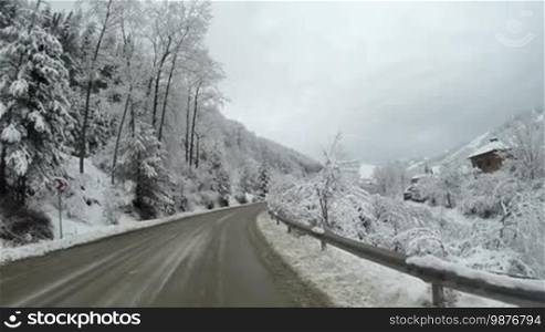 View of an empty road in the mountains during winter with snow-covered trees on the side.