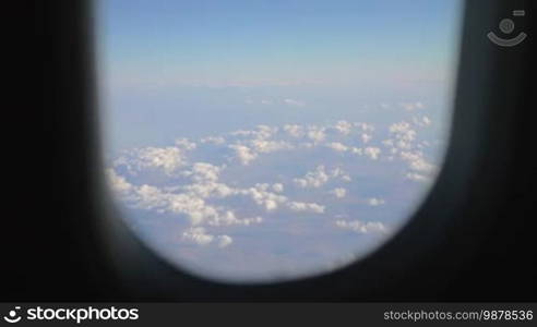 View through the plane illuminator to beautiful white heap clouds over the land. Air travel