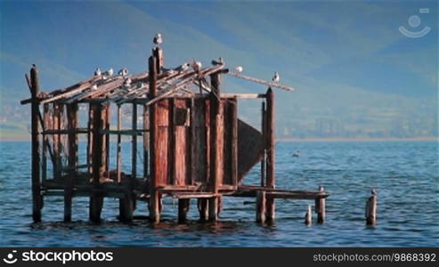 Vintage fisherman house, seagulls on top of it, rippling lake surface, and mountains behind. Dojran Lake, Macedonia.