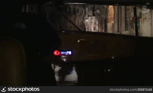 Water tram is carrying passengers along canals in Venice, Italy. Ancient buildings are seen in headlight beam.