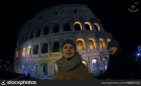 Wide angle shot of happy man and woman making selfie with smartphone in background of Coliseum. Self-portrait against famous Italian landmark in the evening