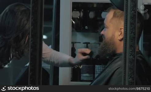 Woman barber trimming beard with electric razor. Man served in barbershop