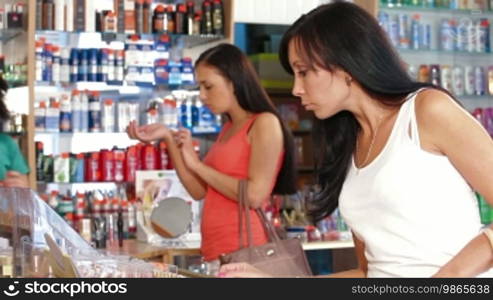 Woman buying lipstick in cosmetics store, seller serving customer in the background