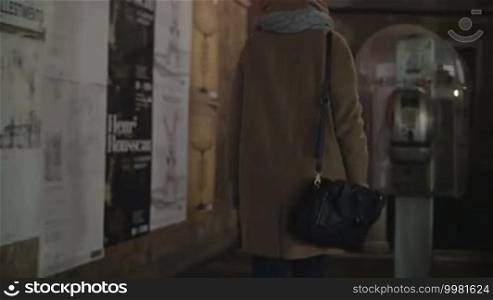 Woman coming up to pay phone, having a talk and then walking in the city at night