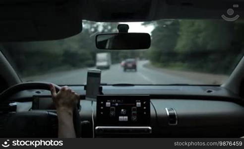 Woman driving car on busy motorway with blurry green forest and traffic in background. View from vehicle's interior. Experienced female driver controlling auto with one hand while traveling by car on highway.