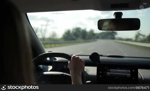 Woman driving car on empty highway on sunny summer day with blurred rural scene on background. View from inside out of vehicle's interior. Young female travelling by auto on motorway.