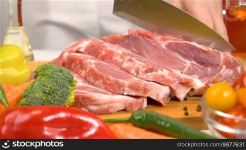 Woman hands slicing fresh raw meat for cooking with vegetables in kitchen. Slow motion shot.