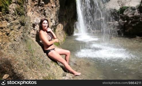 Woman in a bikini on a hot summer day relaxing by the waterfall